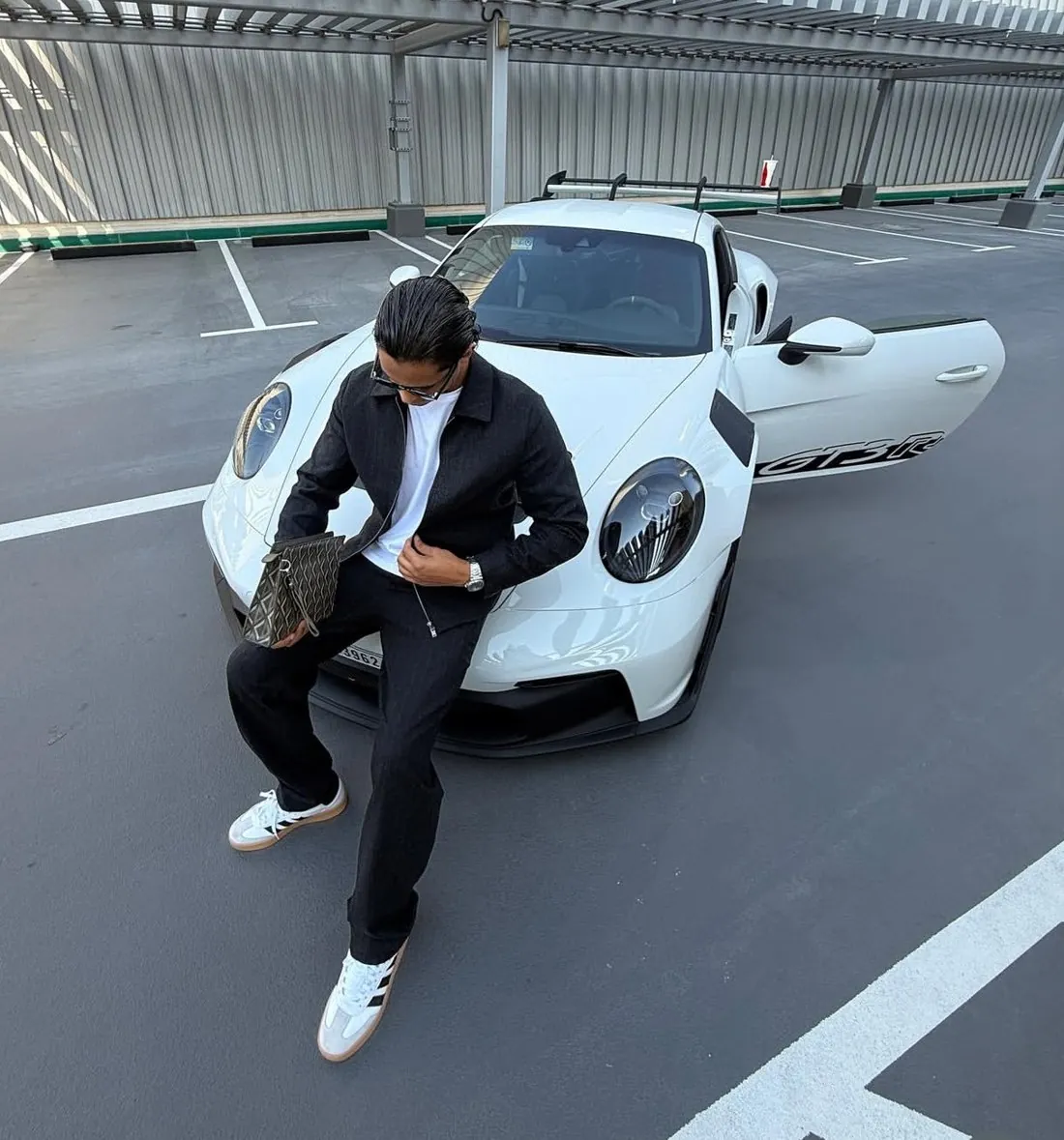 Marwan assis sur le capot d’une Porsche blanche